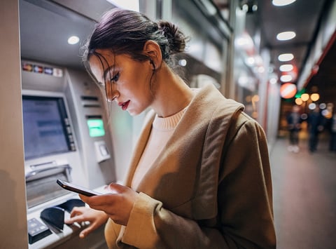 Young woman using ATM machine and smartphone - Nexusmind supports the Banking & Financial Services industry